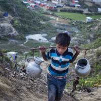 A Rohingya Muslim boy carrying jars full of drinking water walks towardt the Hakim Para refugee camp in Ukhiya, Bangladesh, Monday. | AP