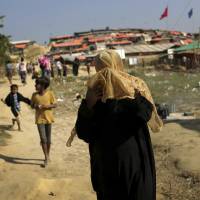 A Rohingya Muslim woman covers her face from the afternoon dust and heat as she walks through the Jamtoli refugee camp on Monday in Bangladesh. | AP