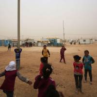 Syrian refugee children play during a sand storm at the Zaatari refugee camp on Monday. Some 80,000 Syrian refugees living in the Zaatari camp will have access to 14 hours of electricity per day instead of eight hours, thanks to the opening of the new solar power station. | AFP-JIJI