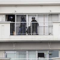 Police officers stand outside a seventh-floor apartment in Kitakyushu on Wednesday where a man with a hunting rifle barricaded himself in and later committed suicide. | KYODO