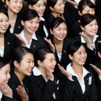 New Japan Airlines Co. employees pose for a photograph after an initiation ceremony at a hangar near Haneda Airport in Tokyo in April. An International Monetary Fund blog says a shift in Japan\'s labor policy would encourage women to take on more full-time work and also have children. | BLOOMBERG