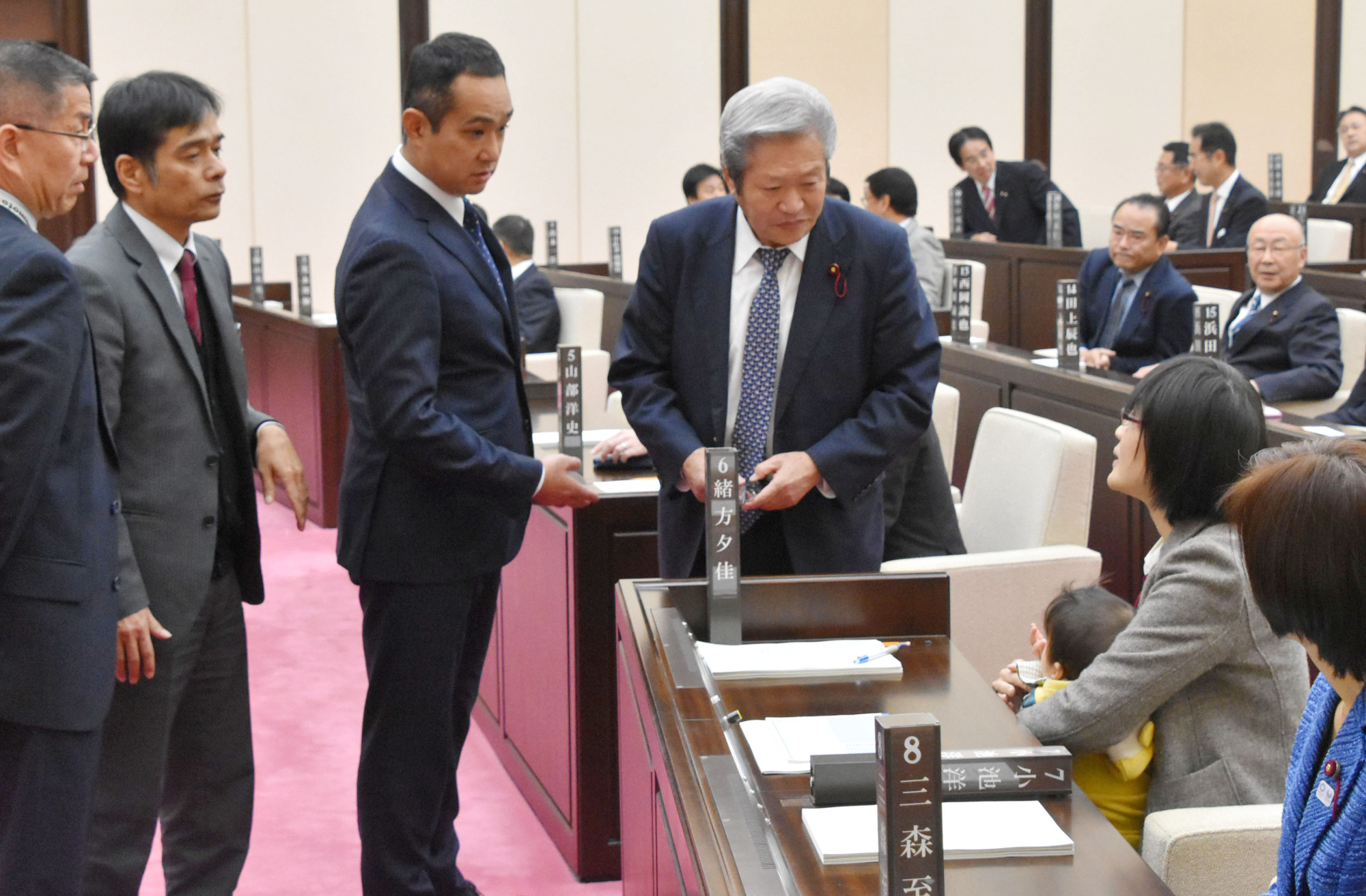 Kumamoto Municipal Assembly member Yuka Ogata holds her 7-month-old baby as her colleagues try to persuade her to leave the chamber last Wednesday. | KYODO