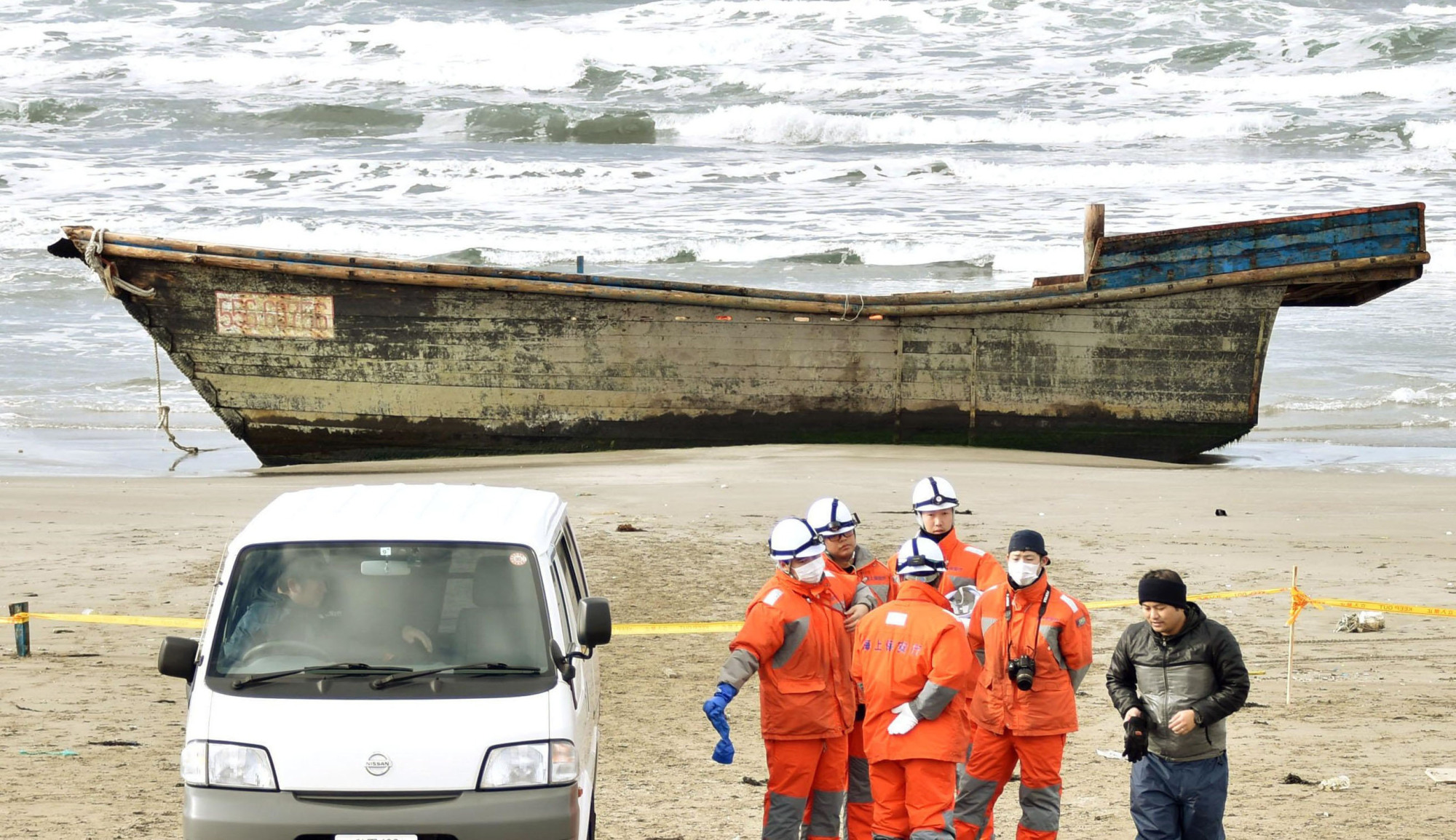 A wooden boat that might have originated in North Korea sits on the beach Monday in Oga, Akita Prefecture. The remains of eight people were found in the boat, which washed ashore Sunday, according to officials at the local branch of the Japan Coast Guard. | KYODO