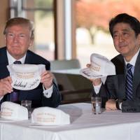 U.S. President Donald Trump holds up a cap as he sits with Prime Minister Shinzo Abe at Kasumigaseki Country Club in Kawagoe, Saitama Prefecture, on Sunday. Trump arrived in Japan earlier in the day, kicking off the first leg of a high-stakes Asia tour. | AFP-JIJI