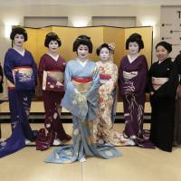 Kikuno (center), her maiko apprentice and three other geisha pose for a photo alongside members of the Hanaakari orchestra in New York. | KOTARO OHASHI
