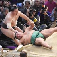 Hakuho (left) and Yoshikaze fall out of the ring during their bout at the Kyushu Grand Sumo Tournament on Wednesday in Fukuoka. | KYODO