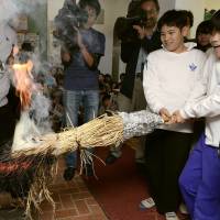 In an event to prepare for winter, students put a sheaf of burning straw into a stone stove at an elementary school in Kobe on Thursday. Usually held on Oct. 23 every year, the school had to postpone the seasonal event this year due to Typhoon Lan. | KYODO