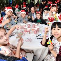 Third-grade students from Nishimachi International School in Tokyo show off ornaments they made from recycled corks. The students are pictured with Grand Hyatt Tokyo General Manager Steve Dewire (center) during the opening ceremony on Tuesday of \"Colors of Hope,\" a Christmas charity program to support children in the disaster-hit Tokuku region and Kumamoto Prefecture. Sixty-four students took part. | YOSHIAKI MIURA