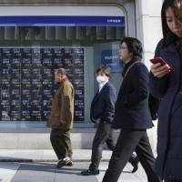 People walk by an electronic stock board outside a securities firm in Tokyo. | AP