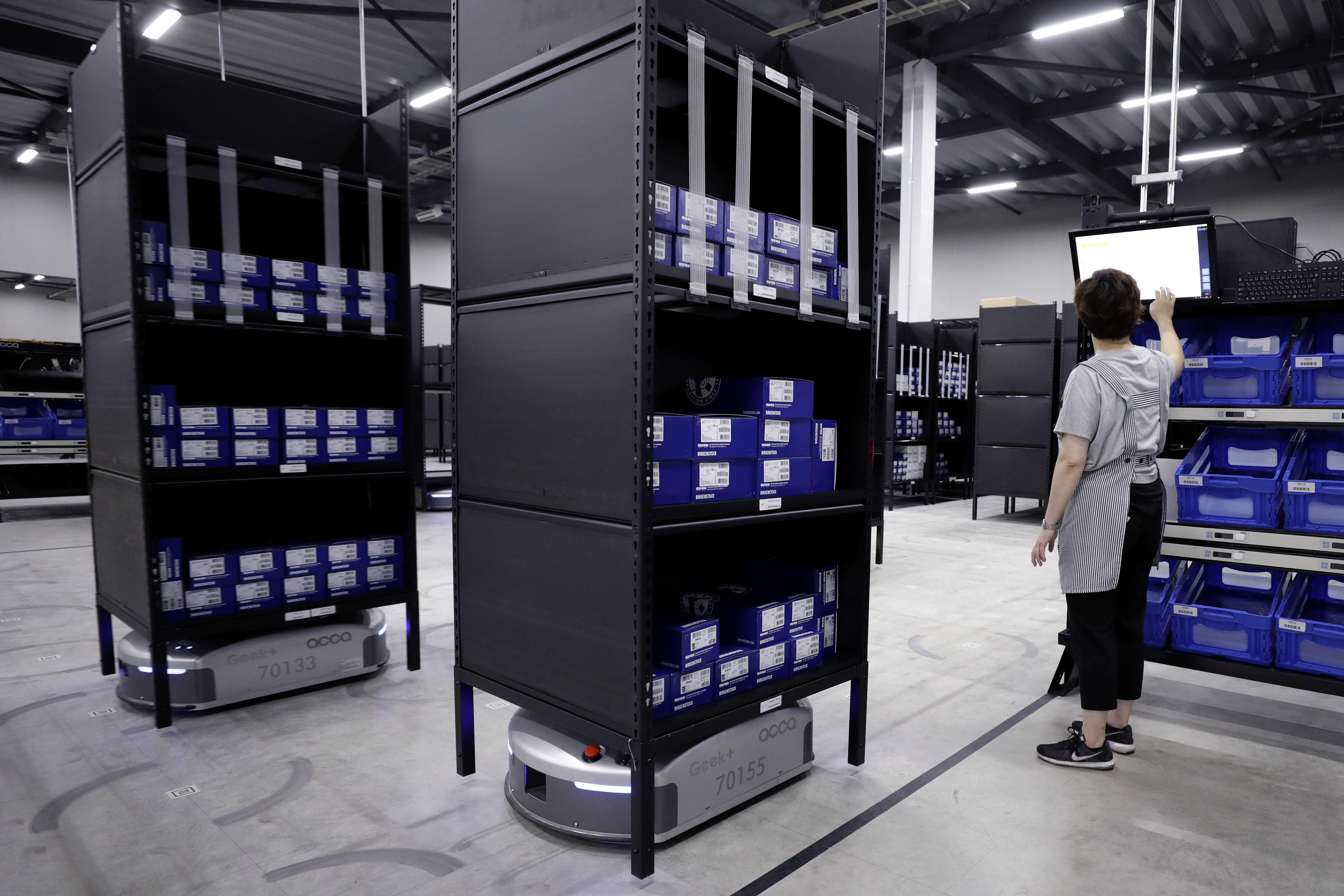 An employee types on a touch screen as a Geek Inc. Eve robot transports shelves at Acca International Co. warehouse in Inzai, Chiba Prefecture, on Sept. 7. | BLOOMBERG