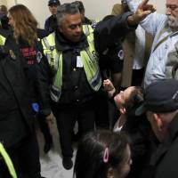 Bekah Bailey (right) of Minneapolis is warned by a Capitol Police officer of arrest unless she and others move on from a hallway where they were protesting the Republican tax overhaul bill Tuesday on Capitol Hill in Washington. | AP