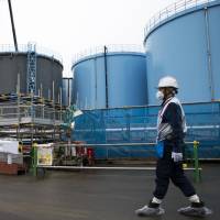 An employee walks past storage tanks containing contaminated water at the Fukushima No. 1 nuclear power plant in Okuma, Fukushima Prefecture, in February. | BLOOMBERG
