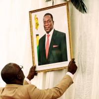 An official hangs a portrait of Zimbabwean President Emmerson Mnangagwa before the swearing-in ceremony of Cabinet ministers at State House in Harare on Monday. | REUTERS