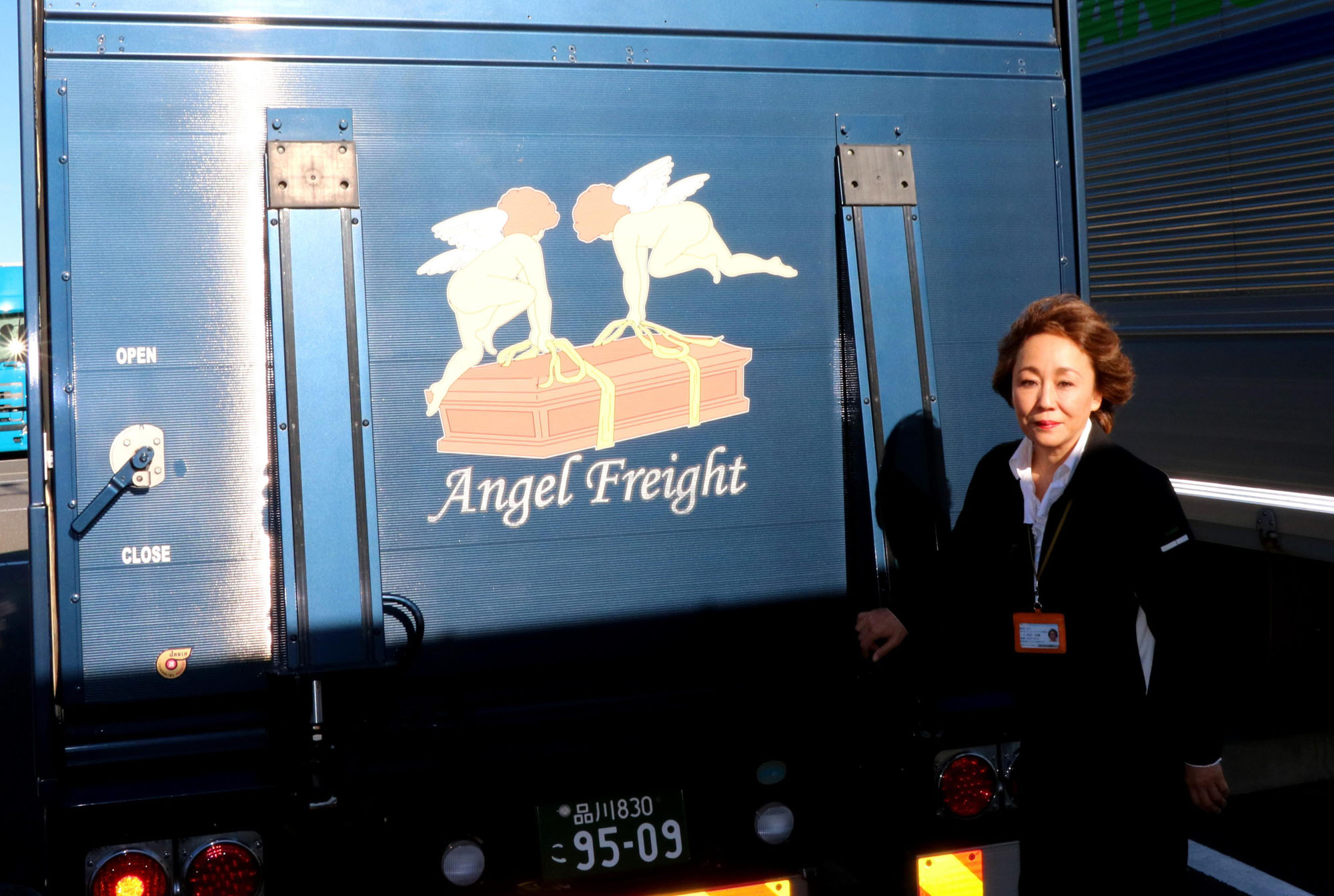 Airhearse International Inc. President Rie Kimura stands next to the company's Angel Freight logo, which appears on the rear door of a truck used as a preparation site for bodies, in the cargo area at Haneda airport in Tokyo on Oct. 23. | KYODO