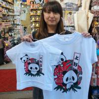 A clerk at a souvenir shop on the Ameyoko shopping street in Ueno holds limited-edition T-shirts of panda cub Xiang Xiang. | CHISATO TANAKA