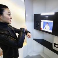 A woman talks to an operator via sign language using a special public phone set up at Haneda airport on Sunday to provide sign-language relay translation services for people with hearing disabilities. | KYODO