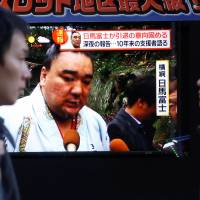People walk past a street monitor showing Sumo grand champion Harumafuji in Tokyo on Wednesday. | REUTERS