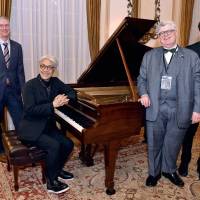 Ryuichi Sakamoto (seated at the piano) attends a reception on Dec. 14 at the Canadian Embassy with (from left) Canadian Ambassador Ian Burney; Brian Levine, executive director of The Glenn Gould Foundation; and electronic musician Scott Morgan. Sakamoto curated \"Glenn Gould Gathering,\" an event marking the 85th anniversary of Glould\'s birth. | YOSHIAKI MIURA