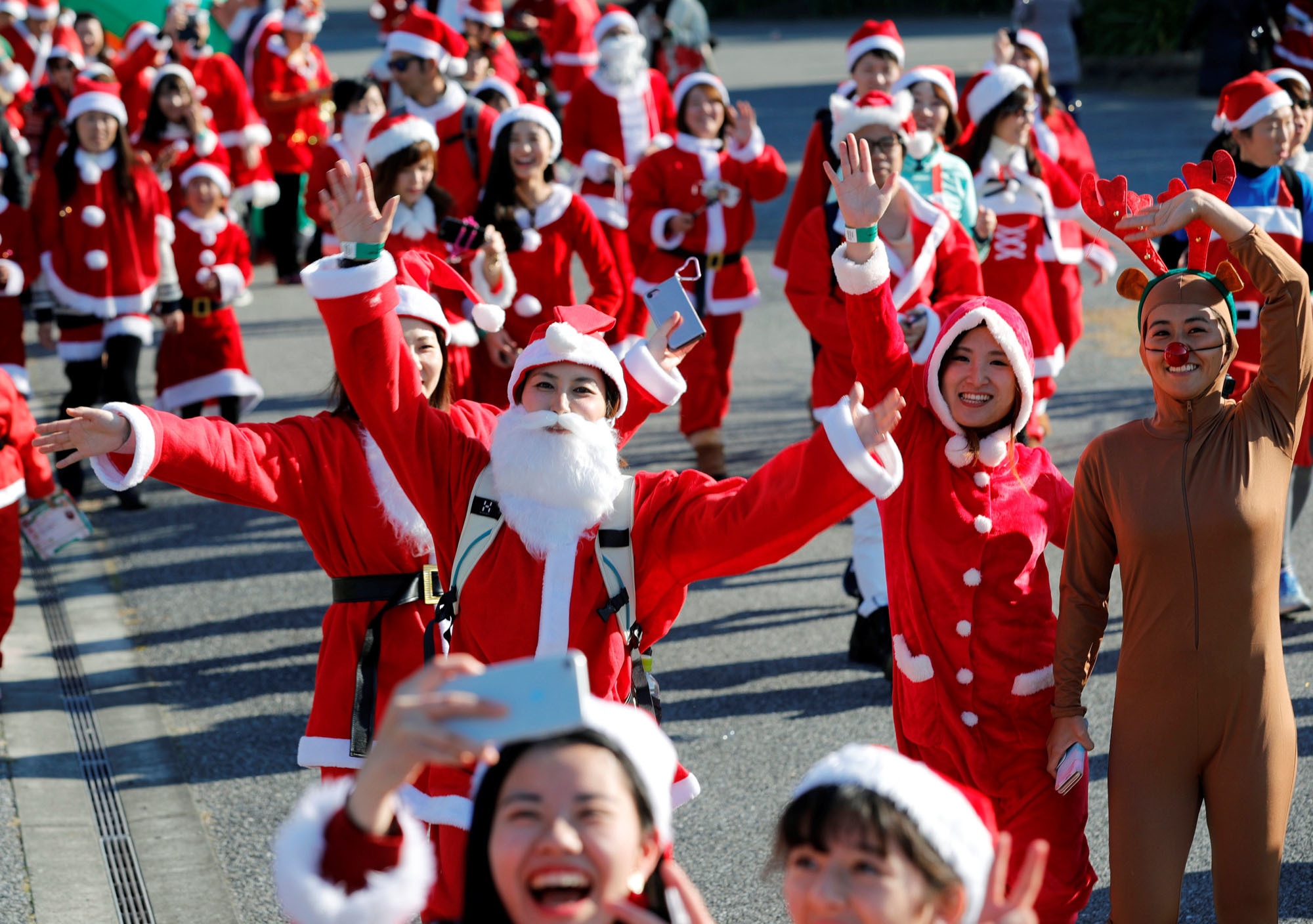 Runners  in Santa Claus outfits wave to a photographer during the annual charity event known as the Tokyo Santa Run in the city of Chiba on Saturday. The entry fees for the run were used to buy presents for children suffering from various diseases. | REUTERS