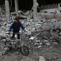 A Syrian boy walks with a bike amid the rubble following reported bombardment by Syrian and Russian forces in the rebel-held town of Hamouria, in eastern Ghouta, on Saturday. Regime and Russian airstrikes on a rebel-held enclave near the Syrian capital killed at least 17 civilians, a war monitor said. | AFP-JIJI