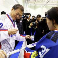 South Korean President Moon Jae-in signs an autograph Wednesday on an ice hockey stick during his visit to Jincheon National Training Center in South Korea. | REUTERS