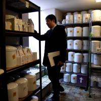 A municipal official checks hundreds of unclaimed urns stored in an underground charnel house in a public cemetery in the city of Saitama. | SATOKO KAWASAKI