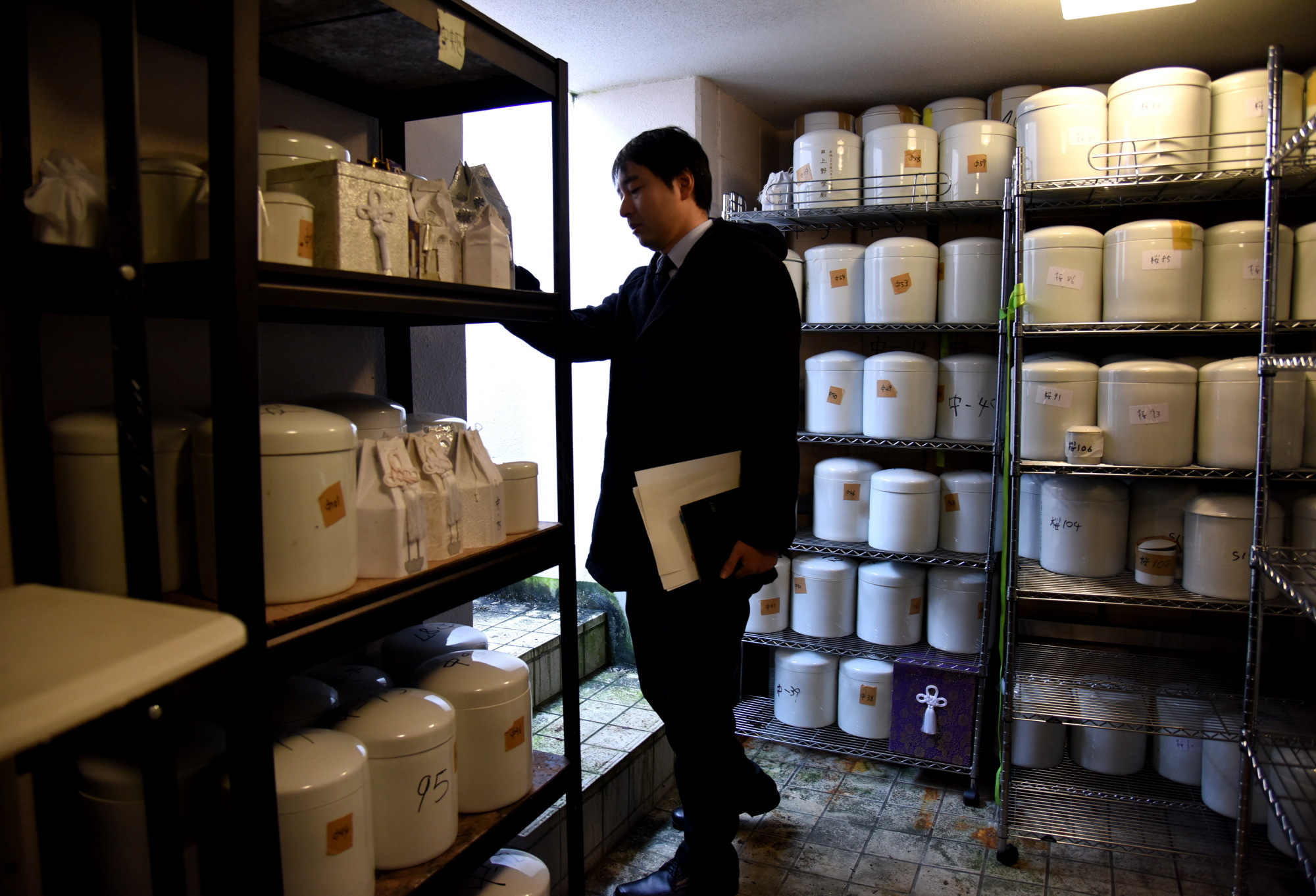 A municipal official checks hundreds of unclaimed urns stored in an underground charnel house in a public cemetery in the city of Saitama. | SATOKO KAWASAKI