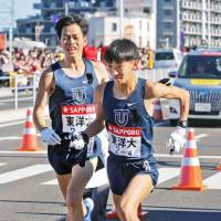Toyo University\'s Hirotsugu Yoshikawa (right) prepares to run the fourth of the Tokyo-Hakone collegiate ekiden on Tuesday, the event\'s first day. Toyo took a 36-second lead into the second day of the 94th edition of the race. | KYODO