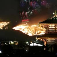 This combination multiple-exposure photo shows Mount Wakakusa in Nara Prefecture awash in fire and fireworks on Saturday. The grass at the foot of the mountain was set alight following a fireworks display in the traditional winter event called \"Wakakusa Yamayaki.\" Heijo Palace\'s Suzaku Gate is seen front right. | KYODO