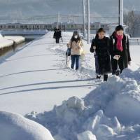 People walk away from a crowded snowbound train on the Shinetsu Line in Niigata Prefecture on Friday morning after spending a long night on board between stations in Sanjo, Niigata Prefecture. | KYODO