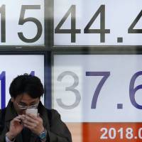 A man looks at a mobile phone in front of an electronic board showing the Nikkei average outside a brokerage in Tokyo on Tuesday morning. | REUTERS
