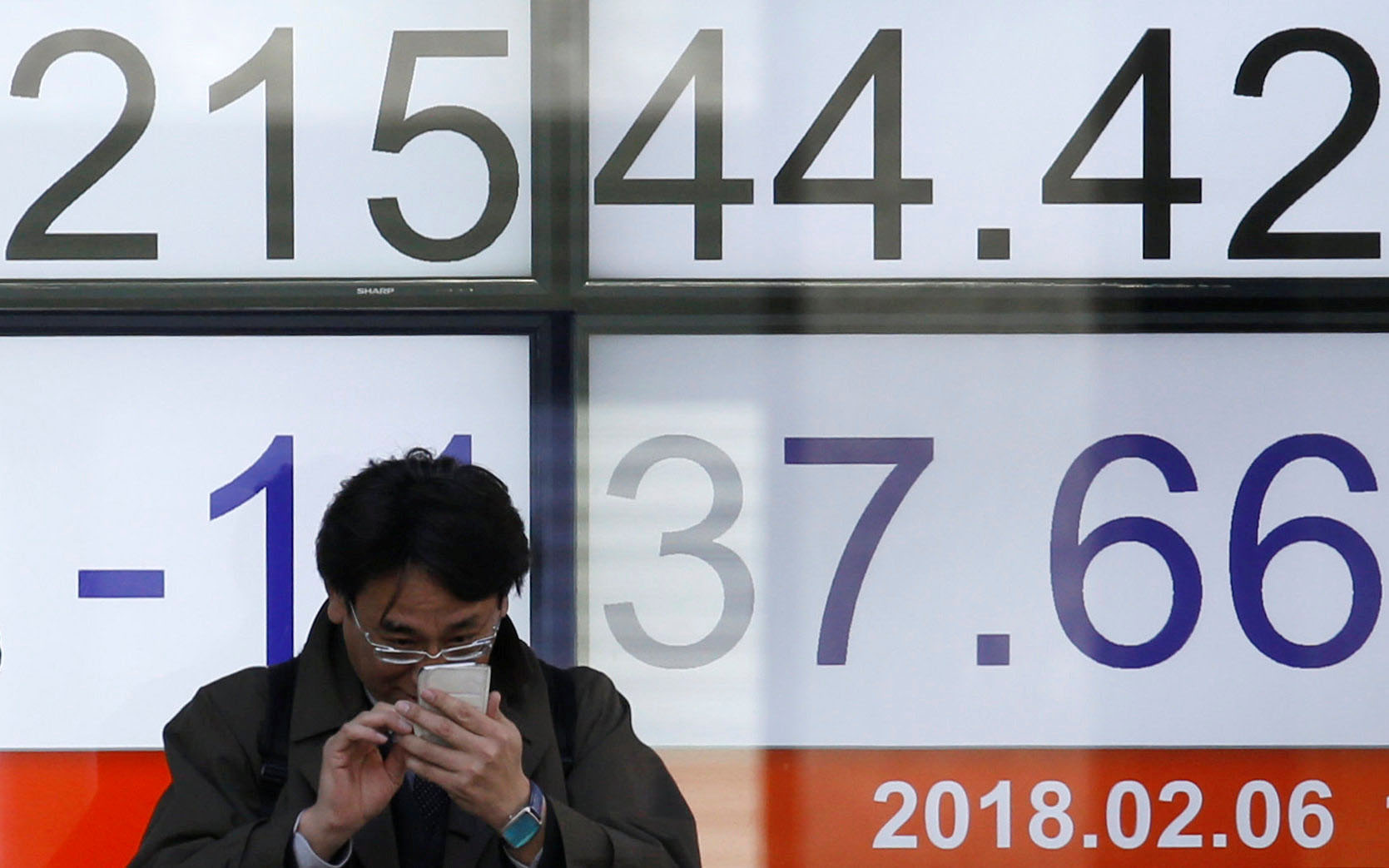 A man looks at a mobile phone in front of an electronic board showing the Nikkei average outside a brokerage in Tokyo on Tuesday morning. | REUTERS