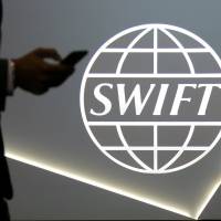 A man using a mobile phone passes the logo of global secure financial messaging services cooperative SWIFT at the SIBOS banking and financial conference in Toronto in October 2017. | REUTERS