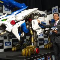 Tomy Co. President Kazuhiro Kojima poses with a large-scale Zoids replica during a news conference in Tokyo\'s Akihabara district on Tuesday. | KAZUAKI NAGATA