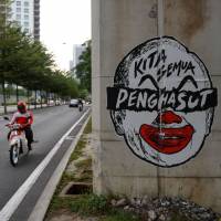 This file photo taken on March 21, 2016 shows a motorcyclist riding past a poster depicting a clown-faced caricature of Malaysian Prime Minister Najib Razak in Kuala Lumpur. | AFP-JIJI