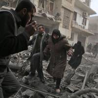 A Syrian civil defense member speaks on a wireless transmitter as other civilians flee an area hit by a reported regime airstrike in the rebel-held town of Saqba, in the besieged Eastern Ghouta region on the outskirts of Damascus on Tuesday. | AFP-JIJI