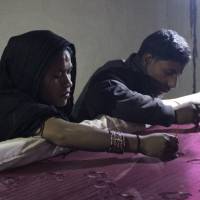 Mohammud Sanu and his wife work on fine needlework by the light of a solar lamp in Pipargaon Nevada, a village in the Indian state of Uttar Pradesh, on Jan. 9. | THOMSON REUTERS FOUNDATION
