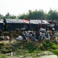 Rohingya refugees collect relief material next to a settlement near the \'no man\'s land\' area between Myanmar and Bangladesh in Tombru in Bangladesh\'s Bandarban on Tuesday. Hundreds of desperate Rohingya Muslims still pour over the Myanmar border into Bangladesh camps every week, six months into the refugee crisis. | AFP-JIJI
