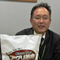 Yutaka Matano of Menicon Co. shows a bag of decomposition accelerant he developed in Nagoya to help Niigata farmers deal with leftover rice straw. | CHUNICHI SHIMBUN