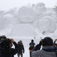 Visitors to the Sapporo Snow Festival on Monday look at an ice sculpture of anime hero Astro Boy in Odori Park. | KYODO