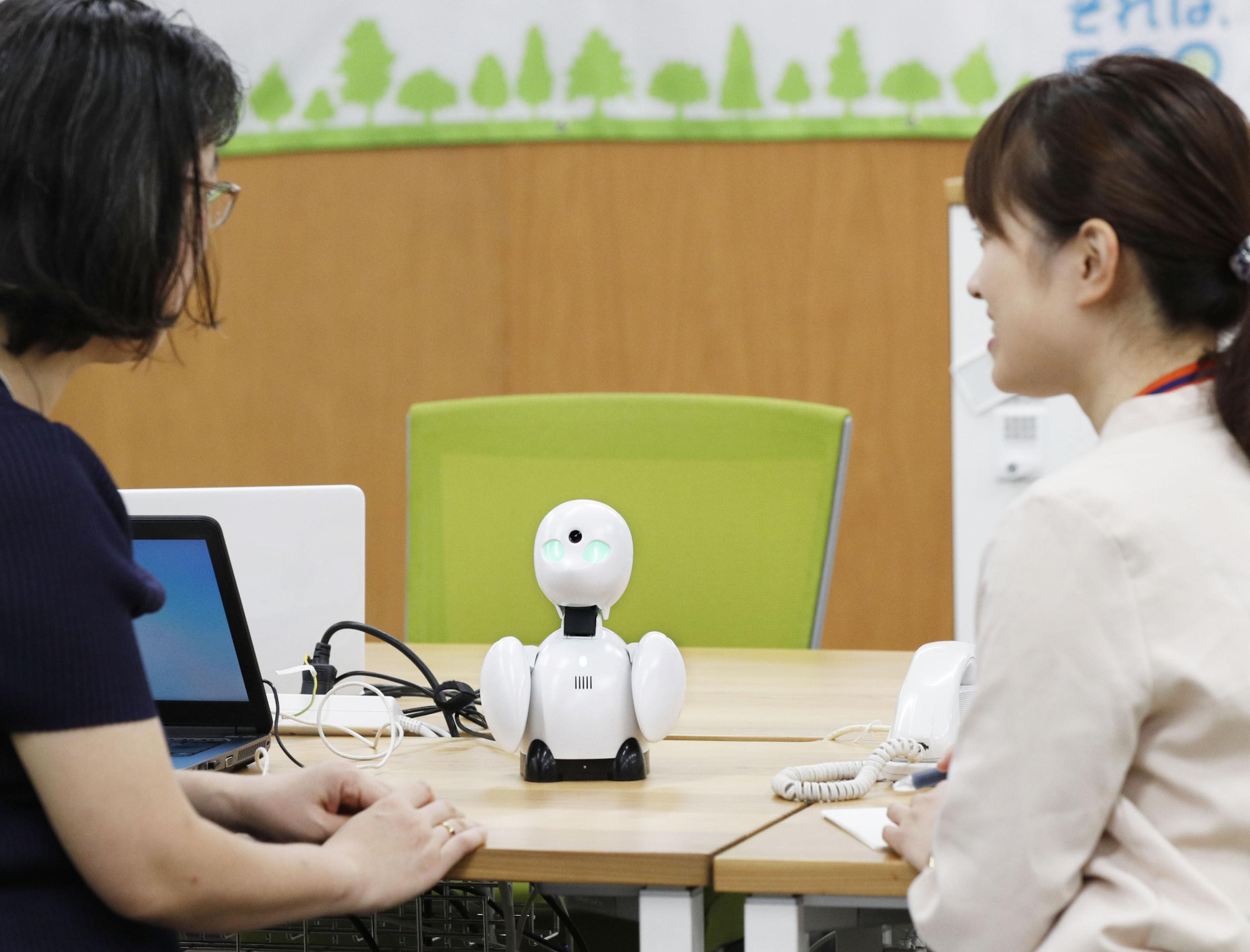 Nippon Telegraph and Telephone East staff members use the OriHime communications robot to talk with an employee working from home in September. | KYODO
