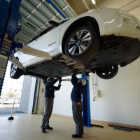 Employees of 4R Energy Corp. work under a Nissan Motor Co. Leaf electric vehicle during a media tour at the company\'s factory in Namie, Fukushima Prefecture, on Monday. | BLOOMBERG