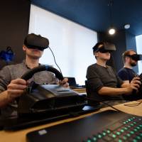 Employees wearing virtual reality headsets use Sony Corp. PlayStation wheel controllers to perform maneuvers within virtual simulations, using Ascent Robotics Inc. Atlas software in Tokyo on Friday. | BLOOMBERG