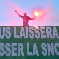 A member of SUD-Rail union holds a flare near a banner reading \"Sud Rail won\'t let you break SNCF\" during a protest over the reform of French national state-owned railway company SNCF in front of the Ground Control venue near the Gare de Lyon in Paris Monday as French rail network celebrates its 80th birthday. French rail workers have agreed to launch a strike starting April 3 against the government\'s plan to overhaul the state-owned operator SNCF, the CGT union said on Thursday. | AFP-JIJI