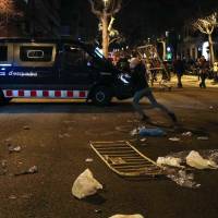 A protestor throws a barrier at a Catalan police van during skirmishes after former regional president Carles Puigdemont was detained in Germany, at a demonstration in Barcelona, Spain, Sunday. | REUTERS