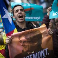 A pro-independence demonstrator holds a poster with of a photo of Carles Puigdemont, the deposed leader of Catalonia\'s pro-independence party, during a protest in Barcelona, Spain, on Sunday. | AP