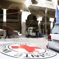 People carry their belonging next to International Red Cross (ICRC) and U.N aid convoys in the besieged Syrian town of Douma, eastern Ghouta, on Friday. | REUTERS