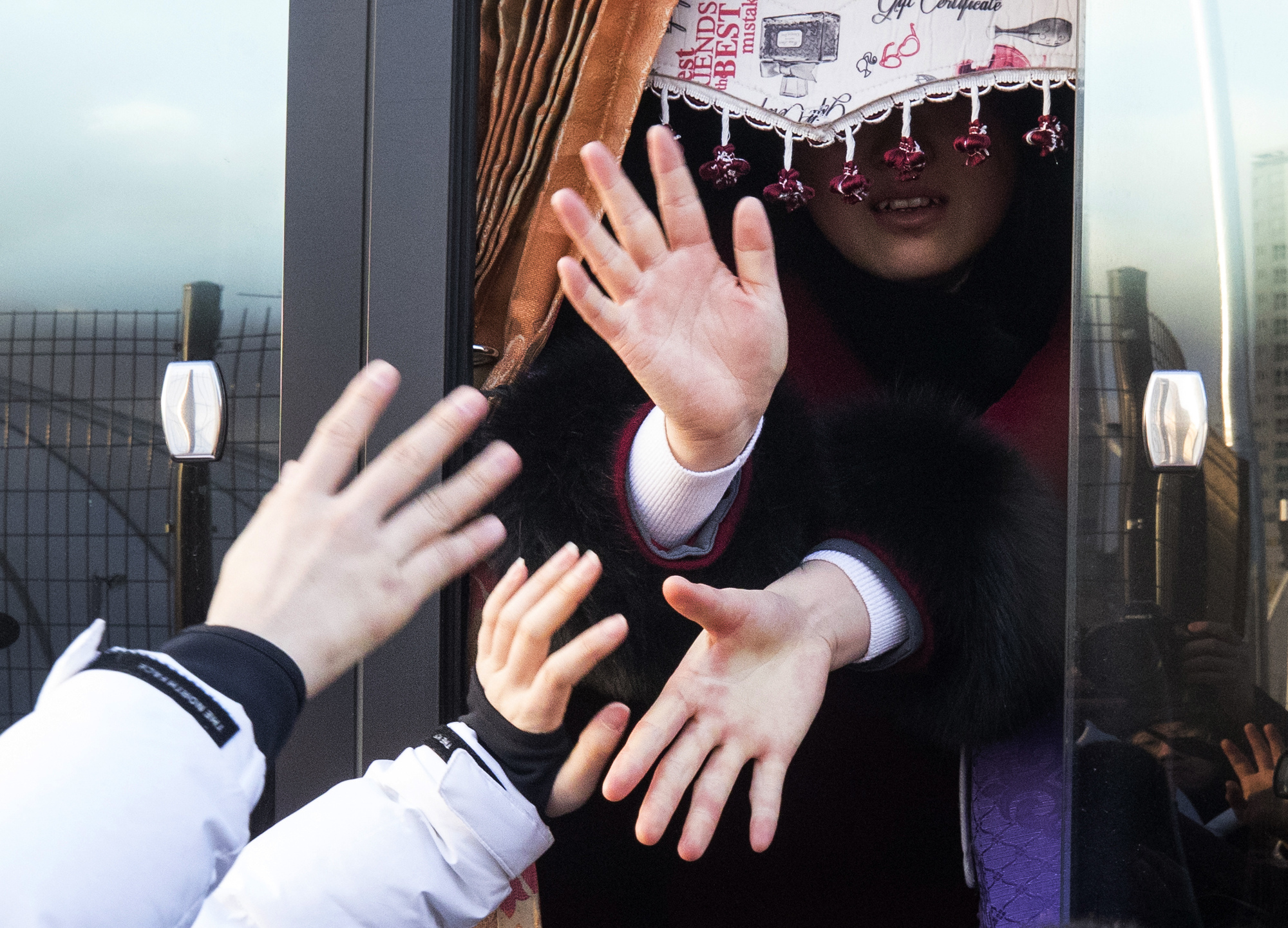 North Korean women's hockey players in a bus reach out to hold hands with their South Korean teammates on Feb. 26, at Olympic Village in Gangneung, South Korea, as they return to North Korea. | AP