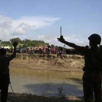 Bangladeshi border guard personnel gesture to Rohingya who are stuck in \"no man\'s land\" as they tell them not to cross in Tombru last August. Some 6,000 Rohingya Muslim refugees who fled attacks in Myanmar last year live at the cloudiest edges of the border with Bangladesh, in a no man\'s land that seems to be neither Myanmar nor Bangladesh. Many stay in these places because they are from nearby villages, and can see the wreckage of their former homes. | AP