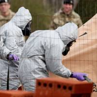 British Military personnel wearing protective coveralls work to remove a vehicle connected to the March 4 nerve agent attack in Salisbury, from a residential street in Gillingham, southeast England on Wednesday. | AFP-JIJI